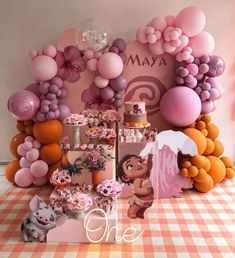 a table topped with lots of pink and orange balloons next to a sign that says moan