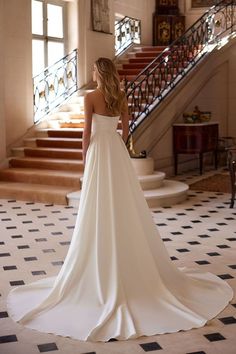 a woman in a wedding dress standing at the bottom of stairs looking off into the distance