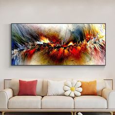 an abstract painting on the wall above a white couch in a living room with red and yellow pillows