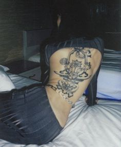 a woman sitting on top of a bed with tattoos on her lower back and legs