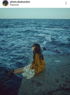 a woman sitting on the edge of a pier next to the ocean