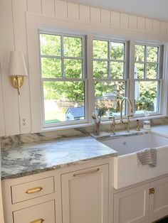 a white kitchen with marble counter tops and gold faucet pulls on the cabinet doors