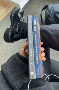 a person is holding a book in their hand while sitting on the floor next to some shoes