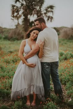 a pregnant couple standing in a field with flowers