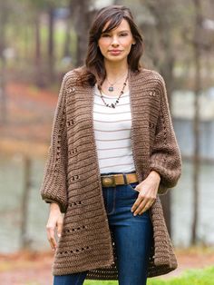 a woman standing in the grass wearing a brown knitted cardigan sweater and jeans