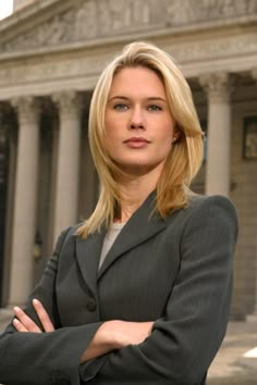 a woman with her arms crossed standing in front of a building and looking at the camera