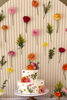 there is a wedding cake with flowers on the wall and behind it are three tiered cakes