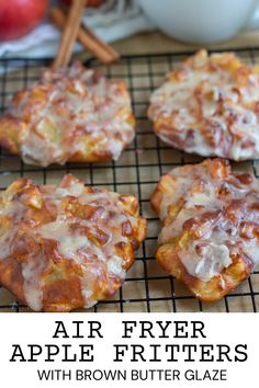 four apple fritters on a cooling rack with cinnamon sticks and apples in the background