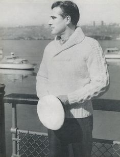 a man holding a frisbee while standing next to a fence near the water