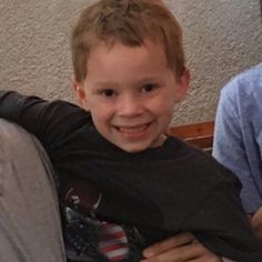 a young boy sitting on top of a couch smiling at the camera with his arm wrapped around him