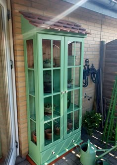 a green china cabinet sitting on top of a patio next to a brick wall and potted plants