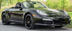 a black sports car parked on the side of the road in front of some trees