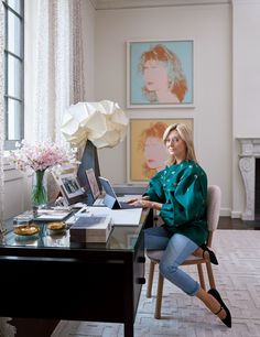 a woman sitting at a desk with a laptop in her lap and flowers on the table