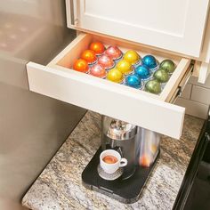 an open coffee maker with colorful balls in it's drawer next to a stove