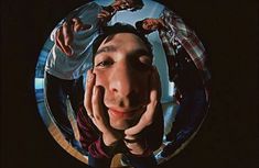 a man with his hands on his face looking at the camera through a circular mirror