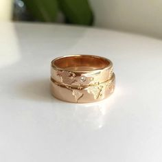 two gold rings with diamonds on them sitting on a white surface next to a green plant