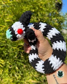 a hand holding a black and white knitted rattler with a red ball in it's mouth