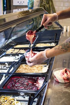 a person cutting up meat on top of a counter next to other food items in trays