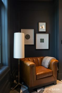 a brown leather chair sitting next to a lamp in a room with pictures on the wall