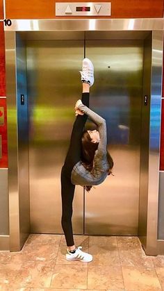 a woman standing on one leg in front of an elevator with her head upside down