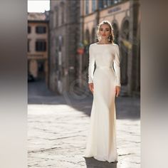 a woman in a white dress standing on a cobblestone street with an old building in the background