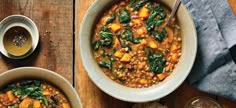 two bowls of stew with spinach, carrots and bread on a wooden table