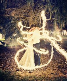 a man and woman are standing in the grass with sparklers on their hands while holding each other