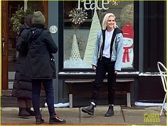 two women walking down the street talking to each other in front of a store window