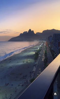 a balcony overlooking the beach at sunset with people walking on it and mountains in the distance