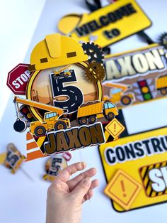 a hand holding up a construction themed cutout with the number five on it and various signs