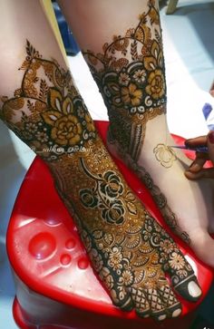 the feet and legs of a woman with henna tattoos on their feet, sitting on a red stool