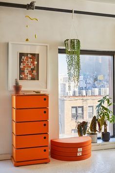 an orange chest of drawers in front of a window with potted plants on it