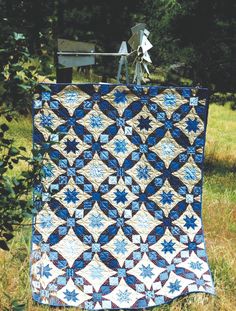 a blue and white quilt hanging on a clothes line in the grass next to a bench