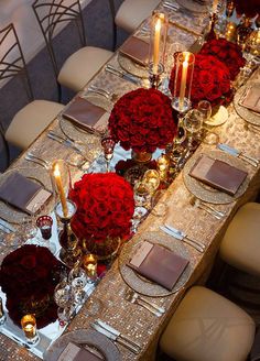 a long table is set with red flowers, candles and place settings for dinner guests