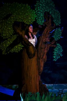 a woman standing on top of a tree in front of a dark background with green leaves