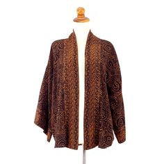 An original design, this beautiful jacket showcases Java's classic batik motifs. Artisan Saktut Raitawati works in brown on black, with matching trim on both sleeves and on the open front for a slimming effect. The batik patterns are created with the silk screen technique. 100% rayon Hand wash separately cold water, dry in the shade Handmade in & fairly traded from Indonesia Due to the handmade nature of this product, exact color, size & pattern may vary. Traditional Brown Outerwear For Fall, Bohemian Brown Kimono For Fall, Bohemian Brown Long Sleeve Kimono, Bohemian Long Sleeve Brown Kimono, Brown Kimono With Kimono Sleeves For Fall, Traditional Brown Kimono For Fall, Casual Long Sleeve Outerwear With Batik Print, Casual Long Sleeve Batik Print Outerwear, Casual Batik Print Outerwear For Fall