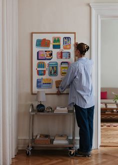 a woman is standing in front of a wall with pictures on it and looking at the floor