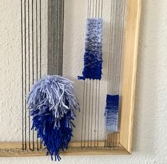 two blue and white yarns are hanging on a wall next to a wooden frame