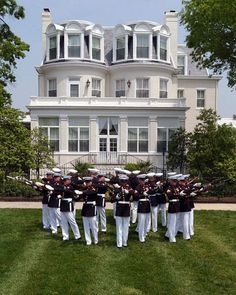 a group of uniformed men standing in front of a large white building with many windows