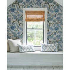 a window seat with two pillows on it in front of a wallpapered room