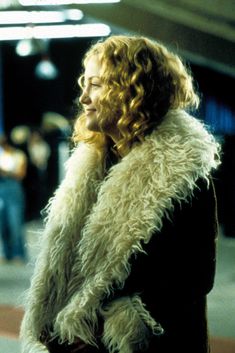 a woman standing on the street talking on her cell phone while wearing a fur coat