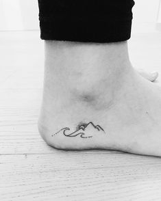 a black and white photo of a person's foot with a mountain tattoo on it