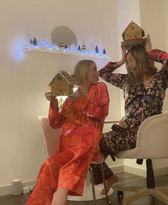 two women are sitting in chairs and one is holding a house on her head while the other holds a doll