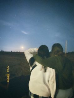 two people are standing in the dark with their arms around each other and looking up into the sky