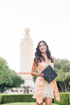 a woman in a graduation gown is holding her diploma and posing for the camera with a building in the background