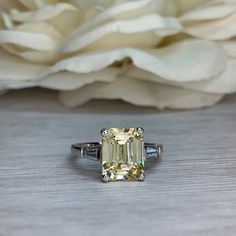 a yellow diamond ring sitting on top of a wooden table next to a white flower