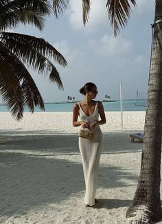 a woman standing under a palm tree on the beach