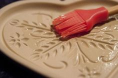 a red brush sitting on top of a white heart shaped dish with ornate designs and leaves