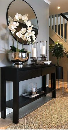 a black console table with white flowers and candles on it in front of a staircase