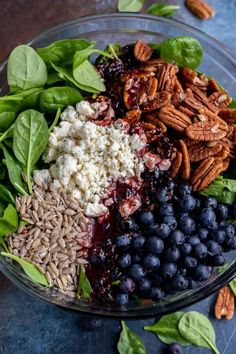 a glass bowl filled with blueberries, spinach, pecans and other ingredients